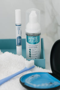 Caneta e espuma claredora junto de escova e alinhador dental em toalha e bandeja.
